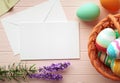 Happy Easter greeting card mockup, blank paper with pastel color eggs, basket, flowers and wooden table. Empty card design Royalty Free Stock Photo