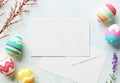 Happy Easter greeting card mockup, blank paper with pastel color eggs, envelope, flowers and wooden table. Empty card design Royalty Free Stock Photo