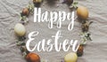 Happy Easter greeting card. Happy Easter text sign handwritten on  Easter eggs and spring flowers wreath on rustic linen, flat lay Royalty Free Stock Photo