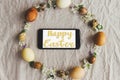 Happy Easter greeting card. Happy Easter text sign handwritten on  phone screen in easter rustic wreath with eggs and flowers flat Royalty Free Stock Photo