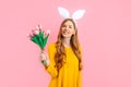 Happy Easter. Happy woman in Easter Bunny ears, girl with a bouquet of tulips, on an isolated pink background Royalty Free Stock Photo