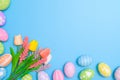 Happy Easter holiday greeting card design concept. Colorful Easter Eggs and spring flowers on blue background. Flat lay, top view Royalty Free Stock Photo