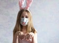 happy Easter. A littel girl with long blonde hair in rabbit ears. She is wearing a medical mask painted with a muzzle