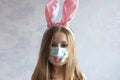 happy Easter. A littel girl with long blonde hair in rabbit ears. She is wearing a medical mask painted with a muzzle