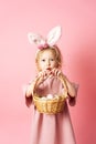 Happy Easter: a little girl in a pink dress and with rabbit ears is holding a basket with colorful eggs in her hands Royalty Free Stock Photo