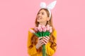 Happy Easter. pensive woman in the ears of an Easter Bunny, a girl with a bouquet of tulips, on an isolated pink background Royalty Free Stock Photo