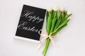 Happy Easter sample text on black chalkboard with tulip flowers on white background. Natural floral spring decorations Royalty Free Stock Photo