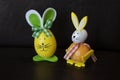 Two easter rabbit figure made of plastic egg, dark background. Green-white and and orange checkered pattern ribbon bow, Yellow-ora Royalty Free Stock Photo