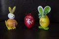 Two easter rabbit figure made of plastic egg, dark background. Green-white and and orange checkered pattern ribbon bow, Yellow-ora Royalty Free Stock Photo