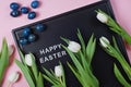 Happy Easter - text on black letter board with white tulips and blue colored eggs on pink background Royalty Free Stock Photo