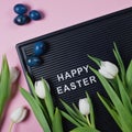 Happy Easter - text on black letter board with white tulips and blue colored eggs on pink background Royalty Free Stock Photo