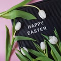 Happy Easter - text on black letter board with white tulips on pink background Royalty Free Stock Photo