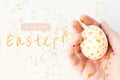 Happy Easter text. Closeup handpainted white egg with gold dots in female hand with gold stars on white background