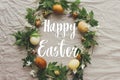 Happy Easter text on Easter eggs and spring flowers wreath on rustic linen, flat lay, handwritten sign. Beautiful stylish greeting Royalty Free Stock Photo