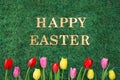 Happy Easter text on green grass with colorful tulips