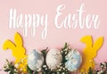 Happy Easter text. Easter greetings card. Stylish easter eggs, yellow bunny, spring flowers on pink paper flat lay. Natural dyed Royalty Free Stock Photo