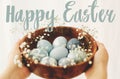 Happy Easter text. Easter greetings lettering. Hands holding wooden bowl with modern blue Easter eggs in spring flowers. Greeting Royalty Free Stock Photo