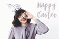 Happy Easter text sign and beautiful girl in bunny ears holding easter egg near face and smiling on white background. Easter hunt Royalty Free Stock Photo