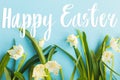 Happy Easter text on white spring snowflakes flowers growing on blue background, handwritten sign. Beautiful stylish greeting card Royalty Free Stock Photo