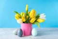 Happy Easter. Wooden decorative eggs and bouquet of yellow tulips in bucket on blue background. Concept: beautiful greeting easter Royalty Free Stock Photo