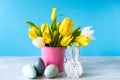 Happy Easter. Wooden decorative eggs, funny bunnie and bouquet of yellow tulips in bucket on blue background. Concept: beautiful