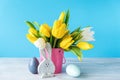 Happy Easter. Wooden decorative eggs, funny bunnie and bouquet of yellow tulips in bucket on blue background. Concept: beautiful Royalty Free Stock Photo