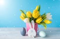 Happy Easter. Wooden decorative eggs, funny bunnie and bouquet of yellow tulips in bucket on blue background. Concept: beautiful Royalty Free Stock Photo
