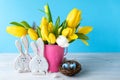 Happy Easter. Wooden decorative two funny  bunnies, eggs in bird nest and bouquet of yellow tulips in bucket on blue background. Royalty Free Stock Photo