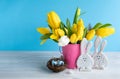 Happy Easter. Wooden decorative two funny  bunnies, eggs in bird nest and bouquet of yellow tulips in bucket on blue background. Royalty Free Stock Photo