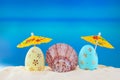 Happy easter. Yellow and blue eggs with conch shell under umbrellas on sandy beach of the sea or ocean Royalty Free Stock Photo