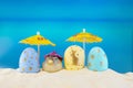 Happy easter. Yellow and blue eggs with puffer fish under umbrellas on sandy beach of sea or ocean Royalty Free Stock Photo