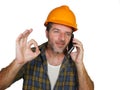 Happy efficient and cheerful workman or contractor man wearing builder hat tallking with satisfied customer on mobile phone