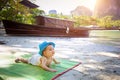 A happy eight month baby crawls along a sandy tropical beach against the background of the sea, mountains and a wooden boat.