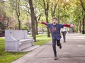 Happy eight year old boy running in a city park with arms stretched out