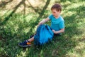 Happy eight-year-old student is sitting on the green grass and opened his backpack