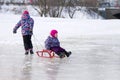 Happy elder sister pulling her young sister on a sled on the ice in snowy winter park Royalty Free Stock Photo