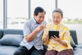 Happy elderly asian couple sitting on couch and using digital tablet computer for online shopping and order food delivery in Royalty Free Stock Photo