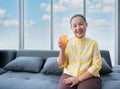 Happy elderly Asian woman sitting on sofa and hold glass of orange juice in living room at home Royalty Free Stock Photo