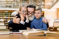 Happy elderly bearded man, grandfather and his cute grandson and granddaughter are sitting at the table in vintage old