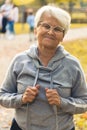 Happy elderly caucasian woman with glasses in gray hoodie portrait in park, autumn day. Vertical shot. Royalty Free Stock Photo