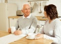 Happy elderly couple drinking coffee in the kitchen while sitting at the table. Royalty Free Stock Photo