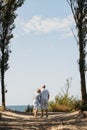 Happy elderly couple hold hands, stand among the trees, look at the sea Royalty Free Stock Photo
