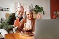 Happy elderly couple man and woman waving at camera while celebrating birthday at home