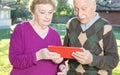 Happy elderly couple reading tablet in the garden, front view Royalty Free Stock Photo