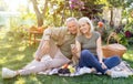 Happy elderly couple relaxing in garden and using smartphone, sitting on blanket on grass, resting outdoors, copy space Royalty Free Stock Photo