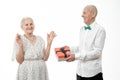 Happy elderly couple, senior man in white shirt present gift box to his old woman in white dress, celebrating birthday Royalty Free Stock Photo