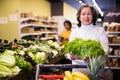 Happy elderly female purchaser with green frisee lettuce in supermarket