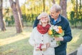 Happy elderly man gives his lady flowers while covering her eyes with palm, she have some present for him Royalty Free Stock Photo