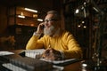 Happy elderly man talking phone while working at home office in evening Royalty Free Stock Photo