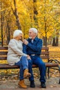 Happy elderly man and woman sitting on a bench in autumn day. Relaxed senior couple sitting on a park bench. Grandfather gently Royalty Free Stock Photo